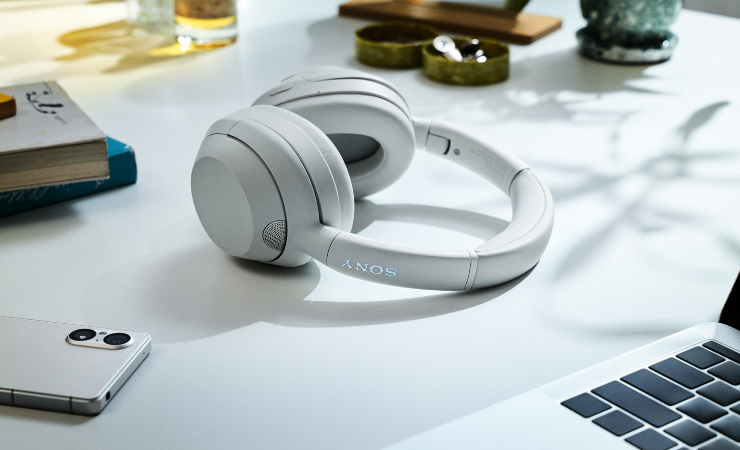 The ULT WEAR headphones in white lying on a busy work surface.