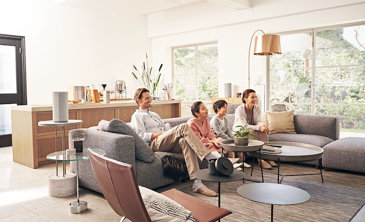 Family on a sofa watching TV with speakers around room creating an immersive experience