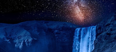 Close up of a waterfall at night with stars illuminated in a galaxy in the sky