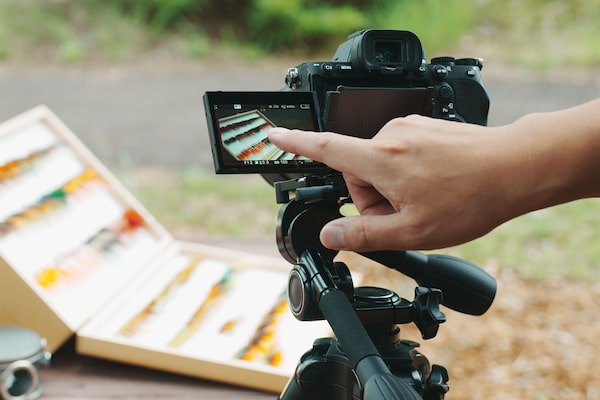 Image of a camera set up at an outdoor shoot, with a man's finger touching the camera's monitor