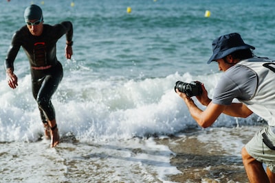 Imagem de utilização de um homem a segurar na câmara para captar um triatleta a sair do mar a correr