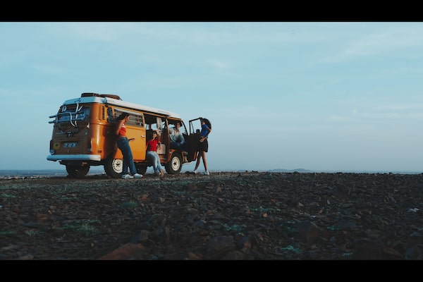 Imagem de exemplo de quatro homens e mulheres a conversar junto a uma carrinha de campismo cor de laranja