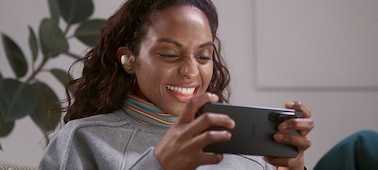 Woman sitting in a living room wearing LinkBuds S, watching video on her smartphone