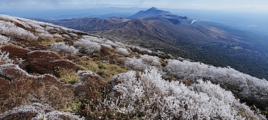 A vast landscape showing a series of mountains. The mountain in the foreground is covered with snow and is in focus